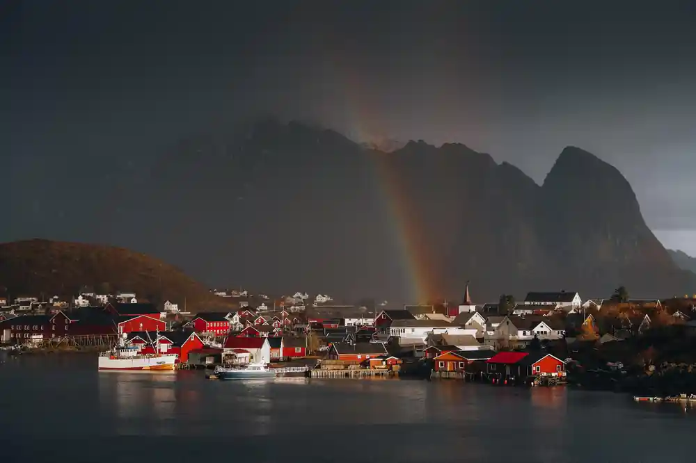 Coastal village with dramatic mountains and rainbow over water