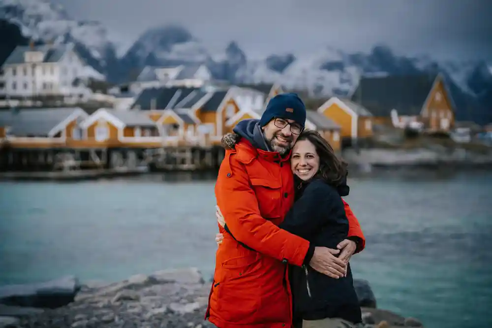 Couple embracing in orange and black coats with snowy mountains behind