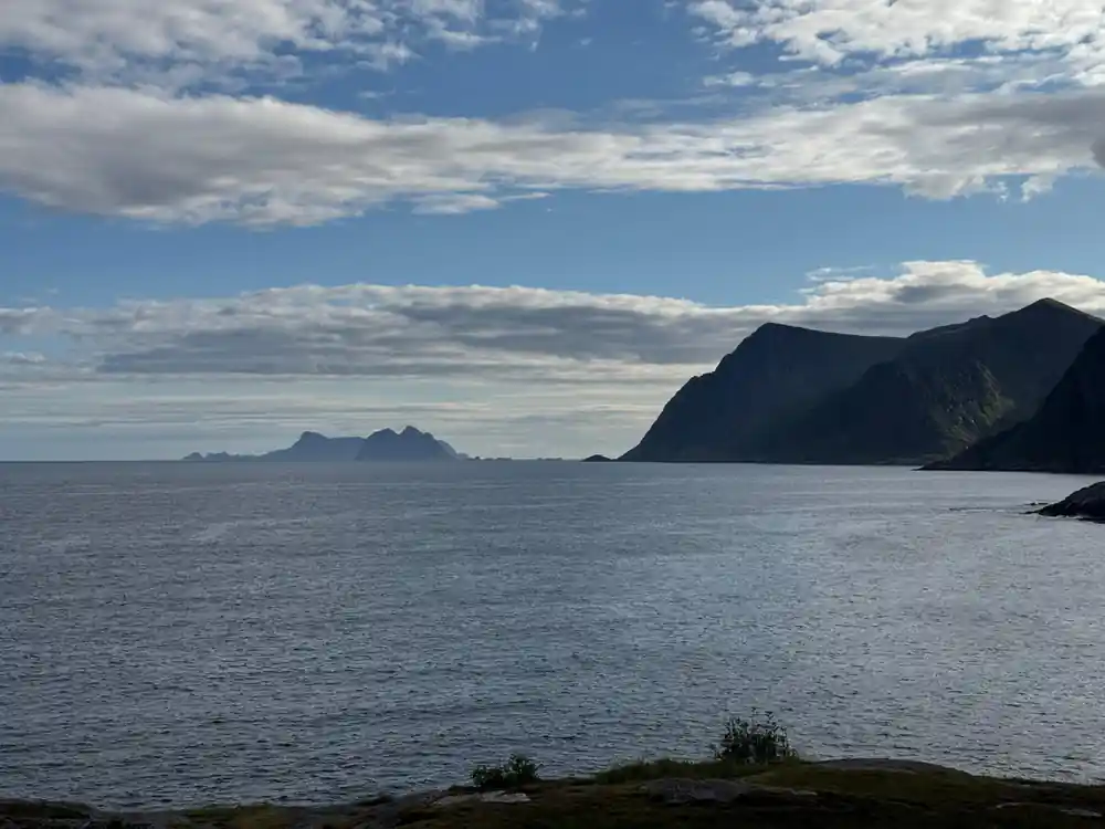 Dark mountains rising from calm blue sea against cloudy sky
