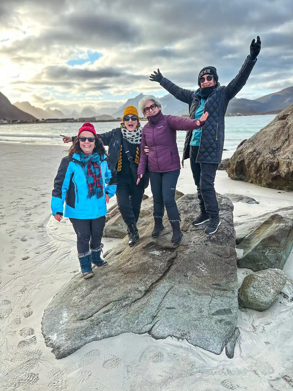 Four people in winter clothing posing on rocky beach with mountains