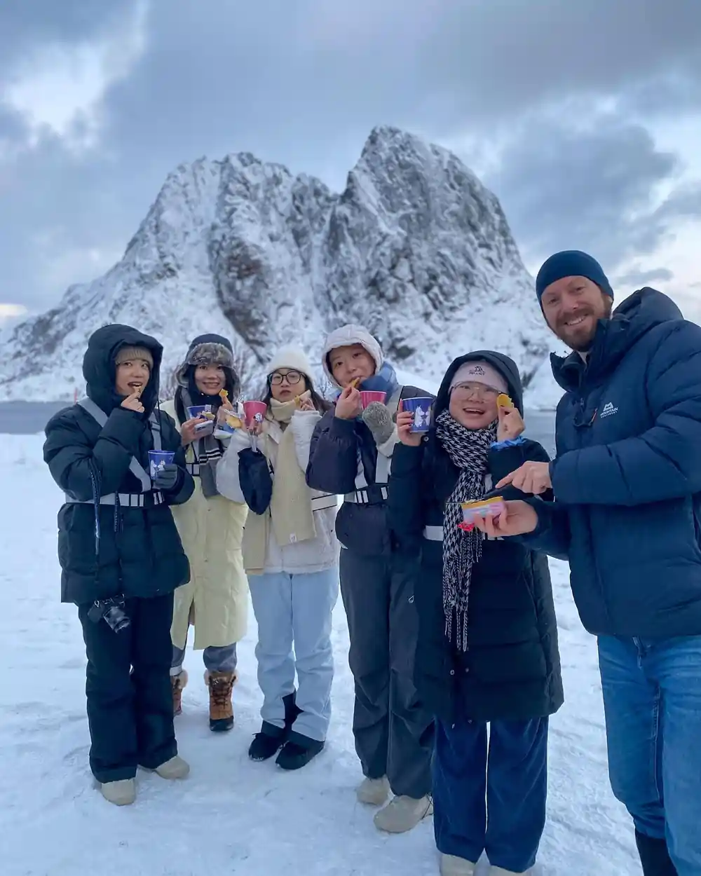 Group of children and adult in winter clothes holding drinks outdoors