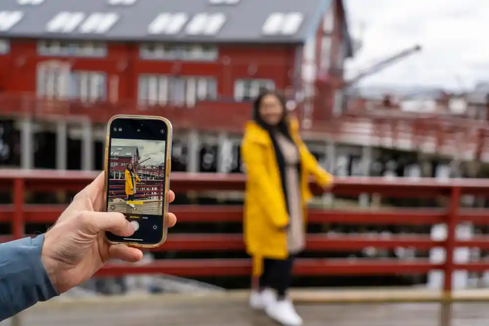 Hand holding phone photographing woman by red wooden fence