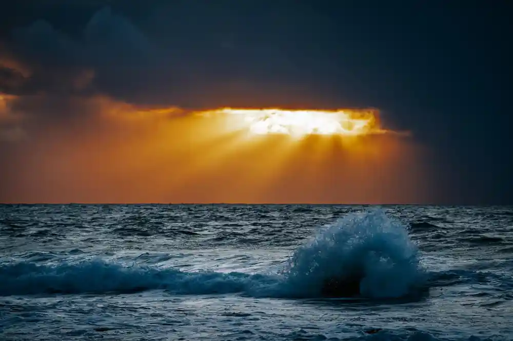 Ocean wave with golden sunlight breaking through dark clouds