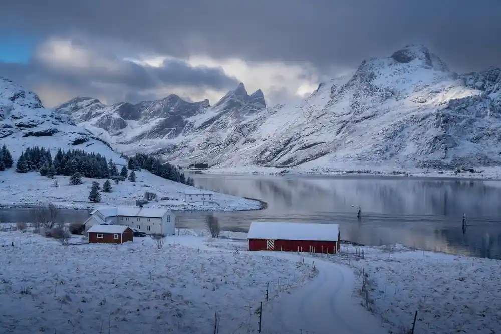 Red cabin on snowy shore with reflected mountains