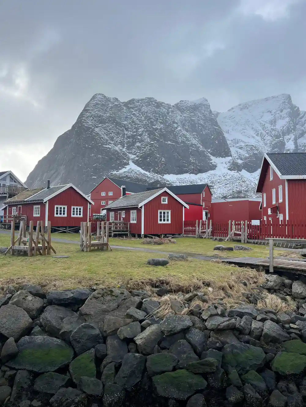 Red cabins in grassy field beneath dramatic rocky peaks