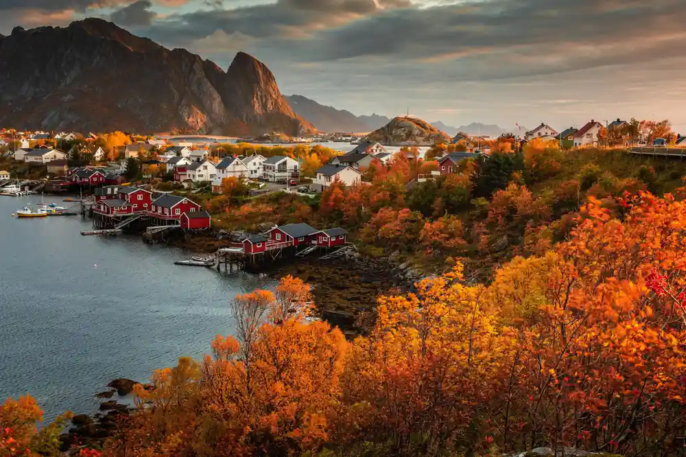 Red fishing huts in autumn forest with steep mountain backdrop