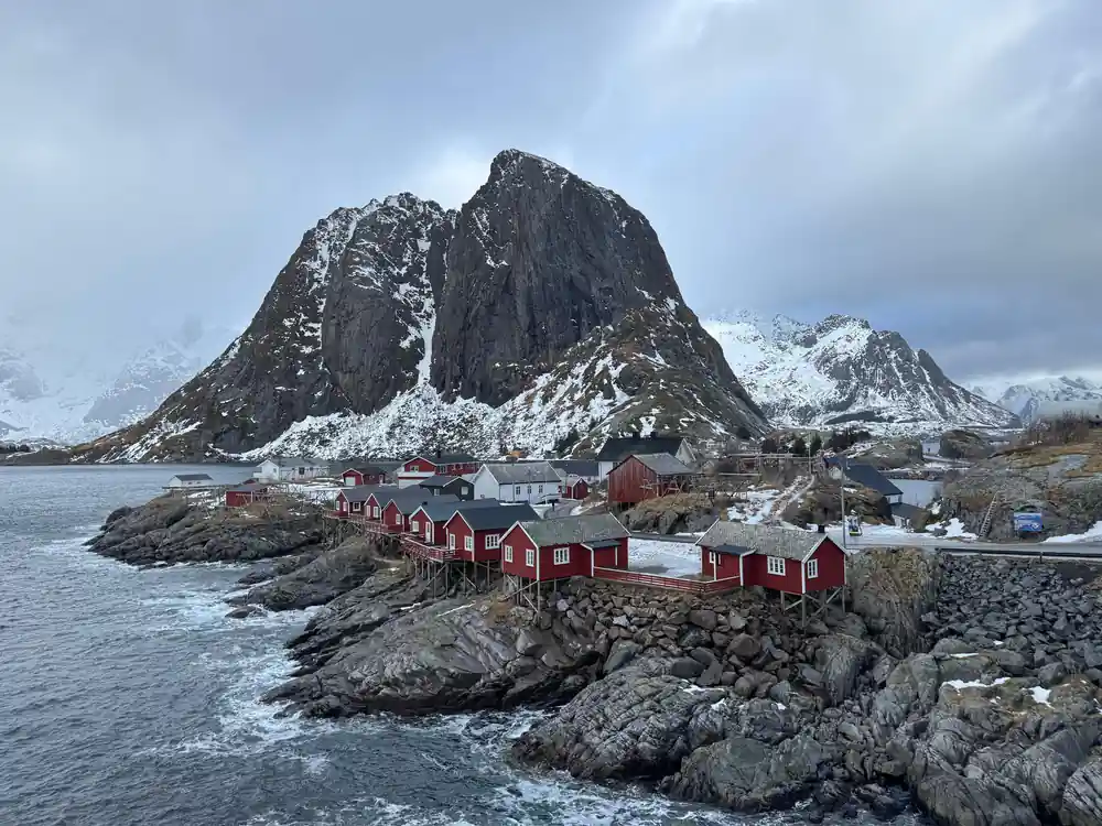 Red fishing huts on rocky island with dramatic mountain backdrop