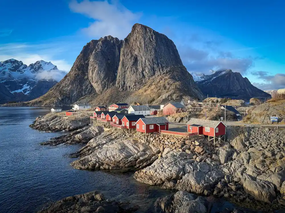 Red fishing huts on rocky shore beneath steep mountain peak