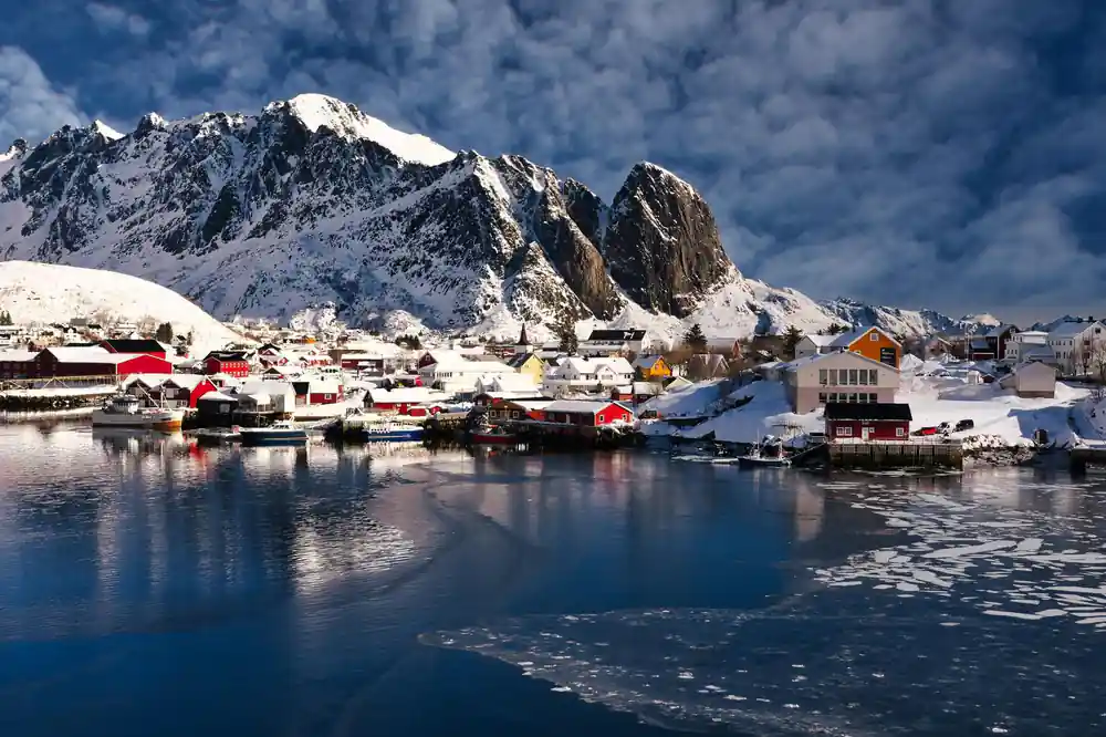 Red and white buildings on waterfront with snowy peaks