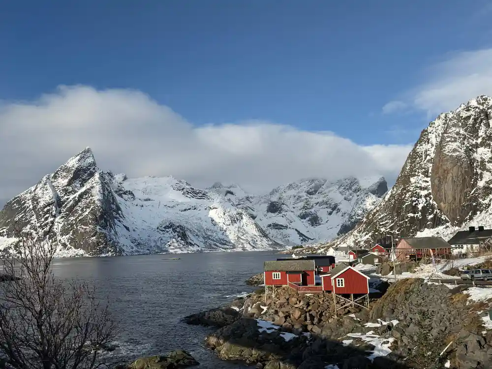 Red wooden cabins on rocky shore by snowy mountains