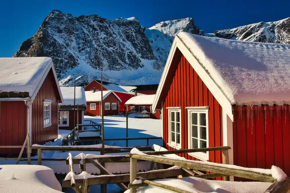 Red wooden houses with snow and jagged mountain peak in background