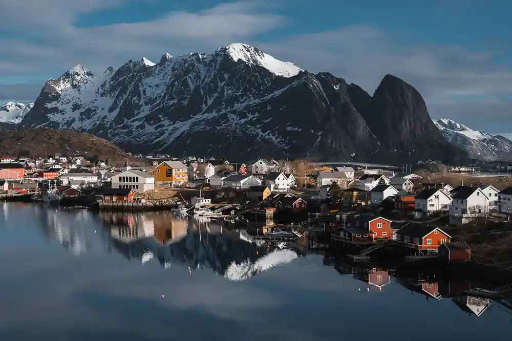 Snow-capped mountain peak reflected in calm water with colorful waterfront village