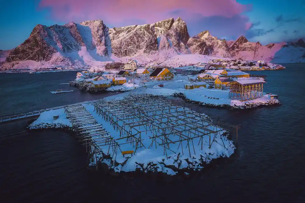 Snow-covered fish farm racks with pink-lit mountains at dusk