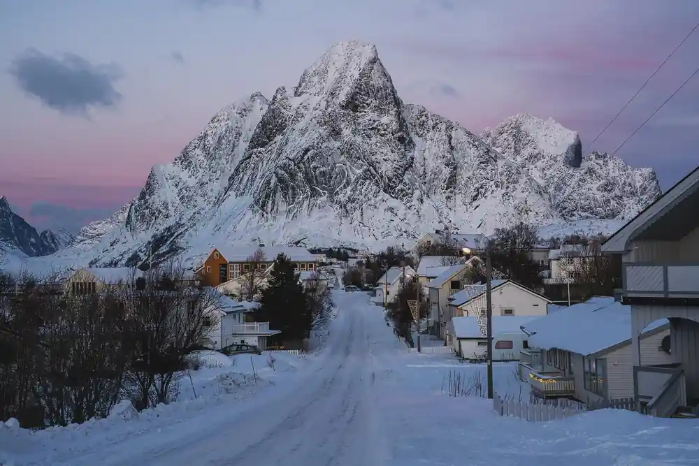Snowy road through village with dramatic mountain backdrop