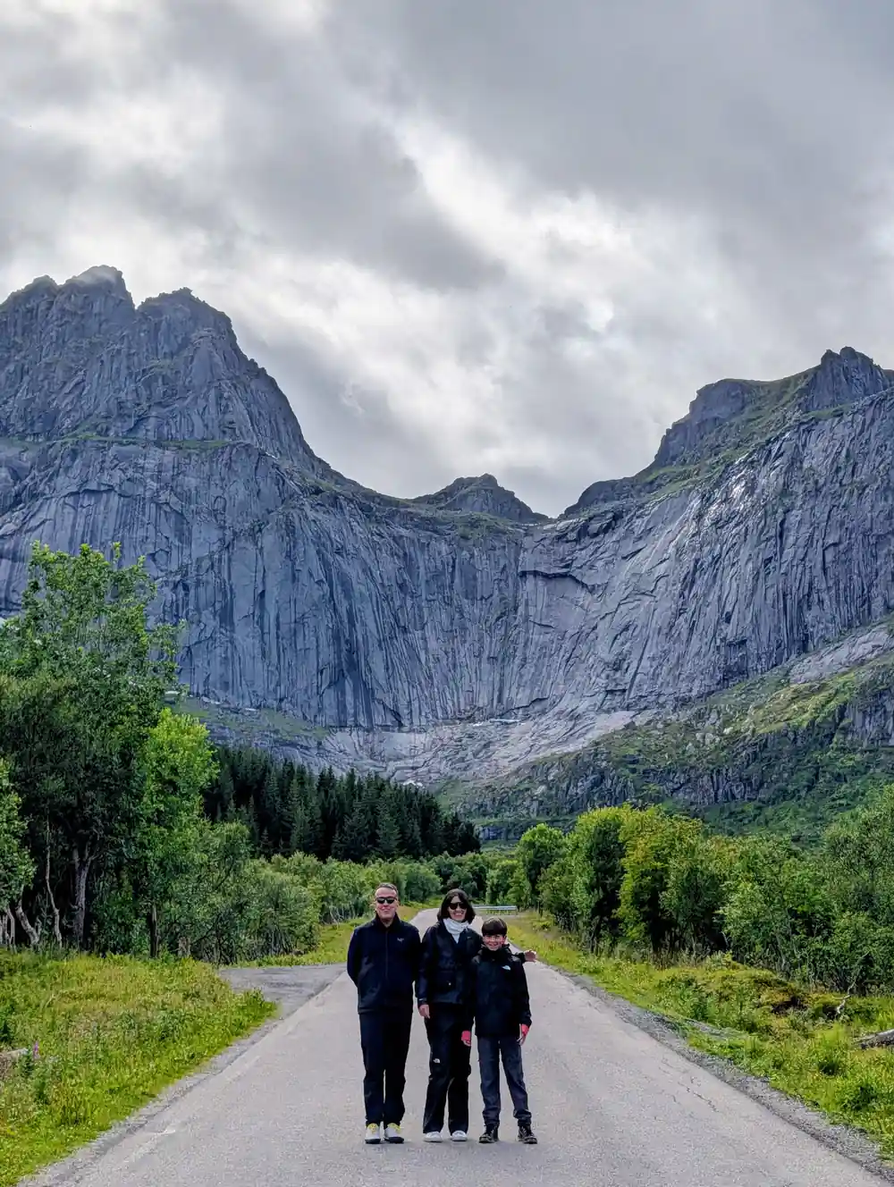 Three people standing on straight road between mountains