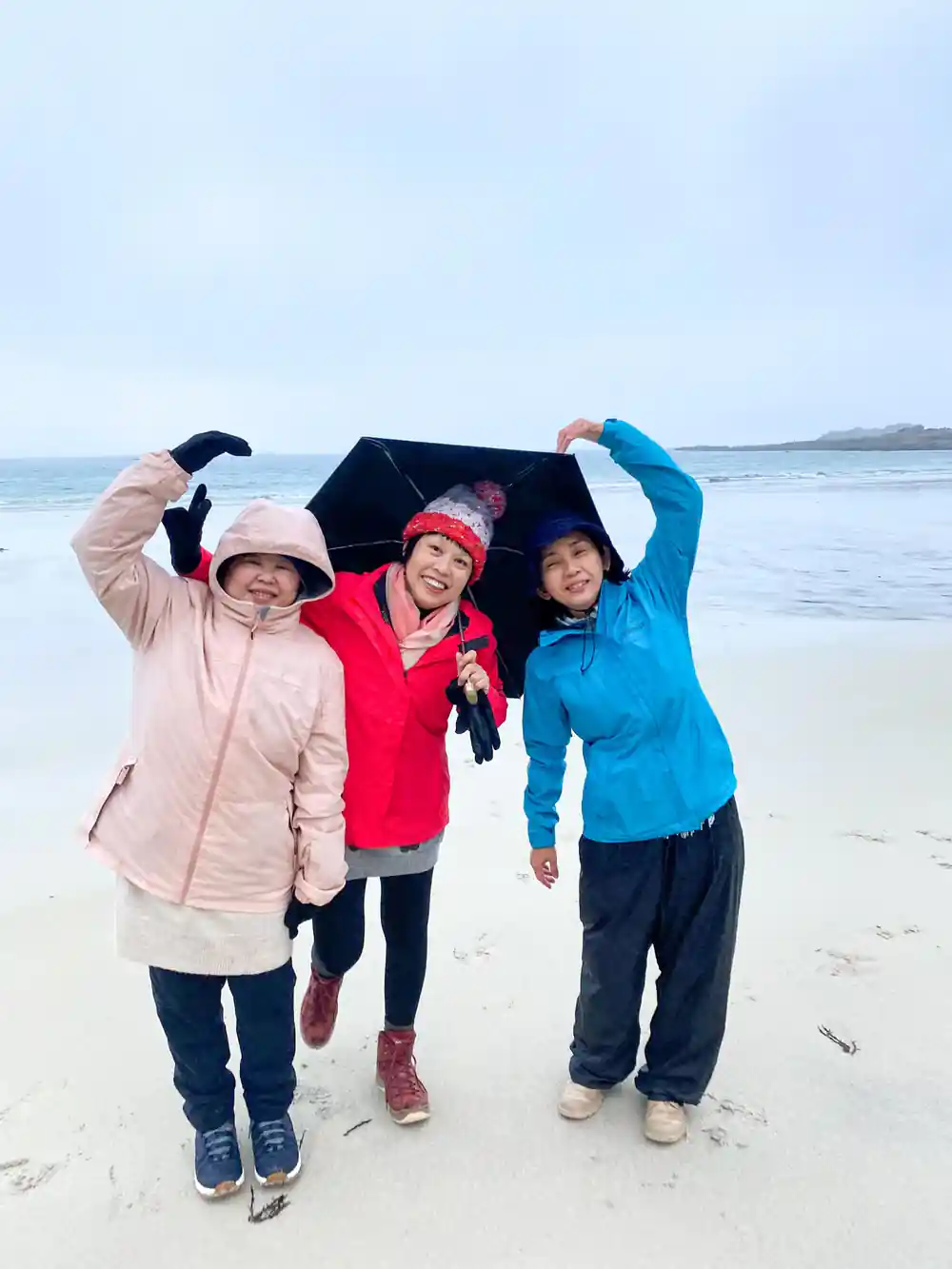 Three women on beach holding up fabric in windy conditions