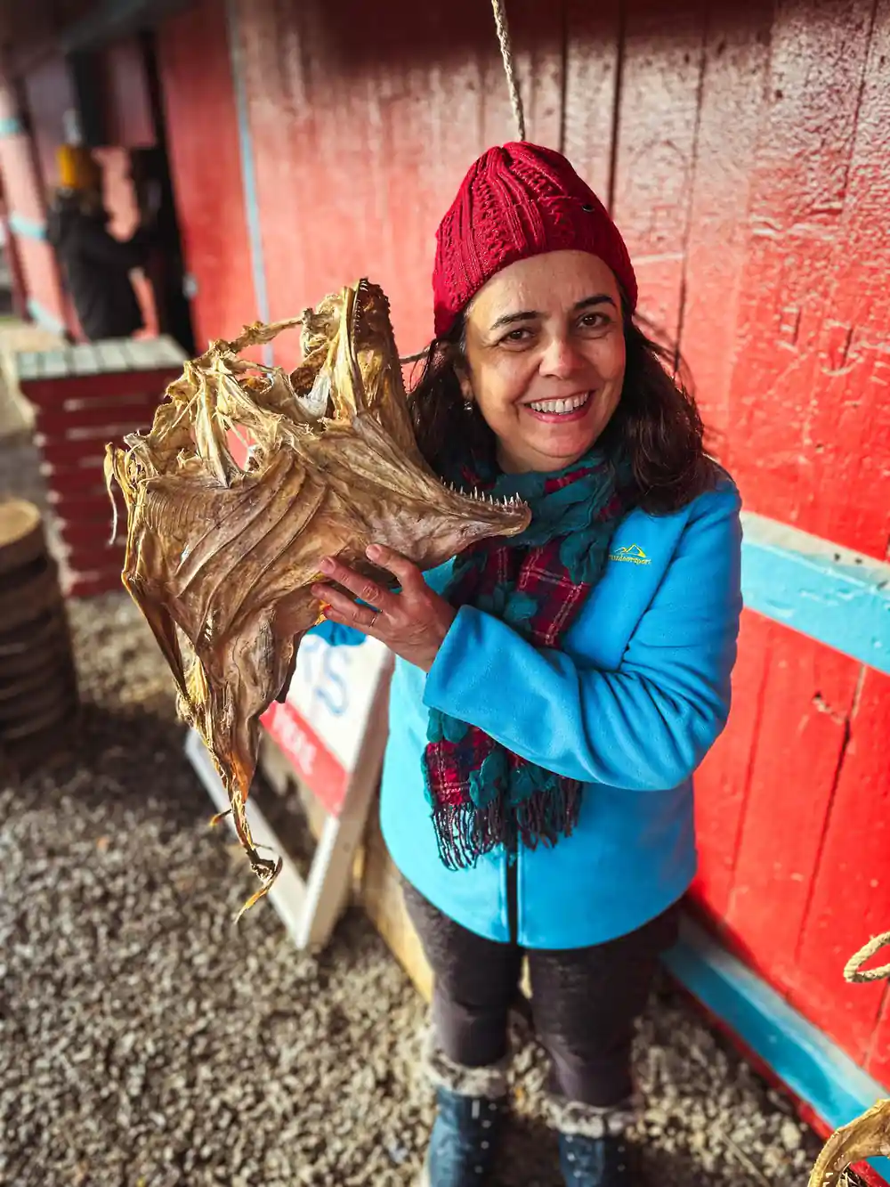 Woman holding dried fish wearing red hat and blue jacket