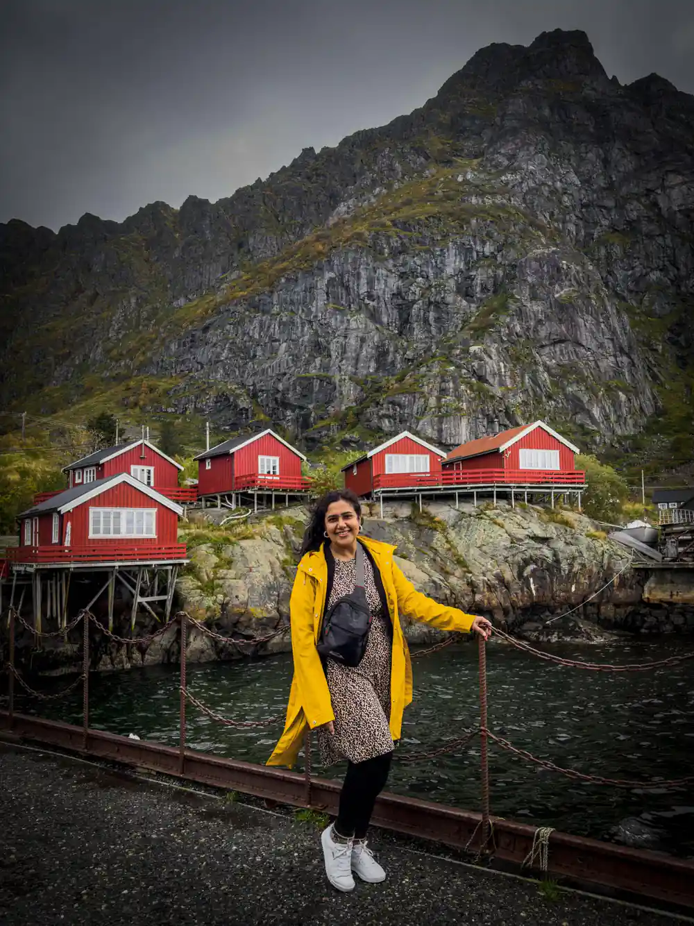 Woman in yellow jacket poses by red waterfront buildings