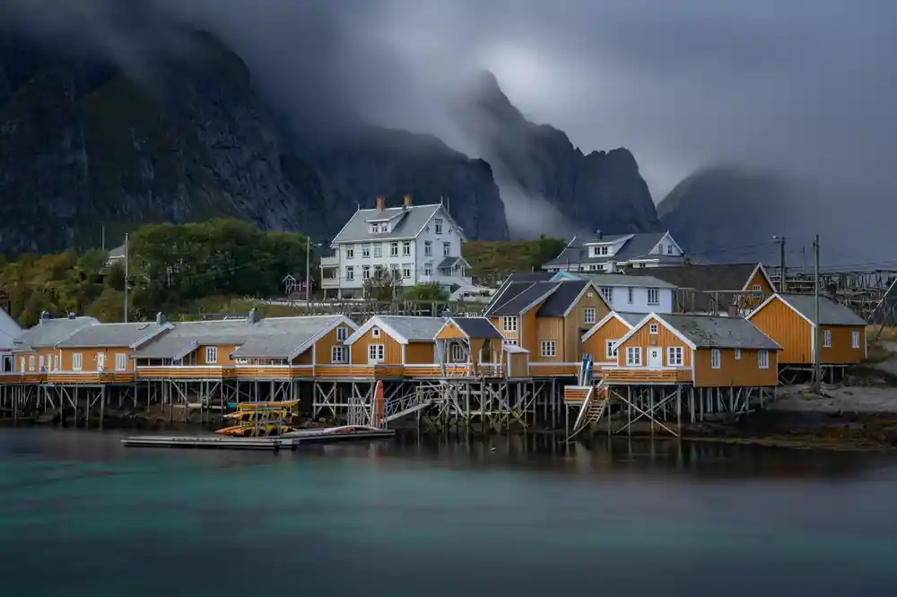 Yellow and white houses on stilts beside misty fjord