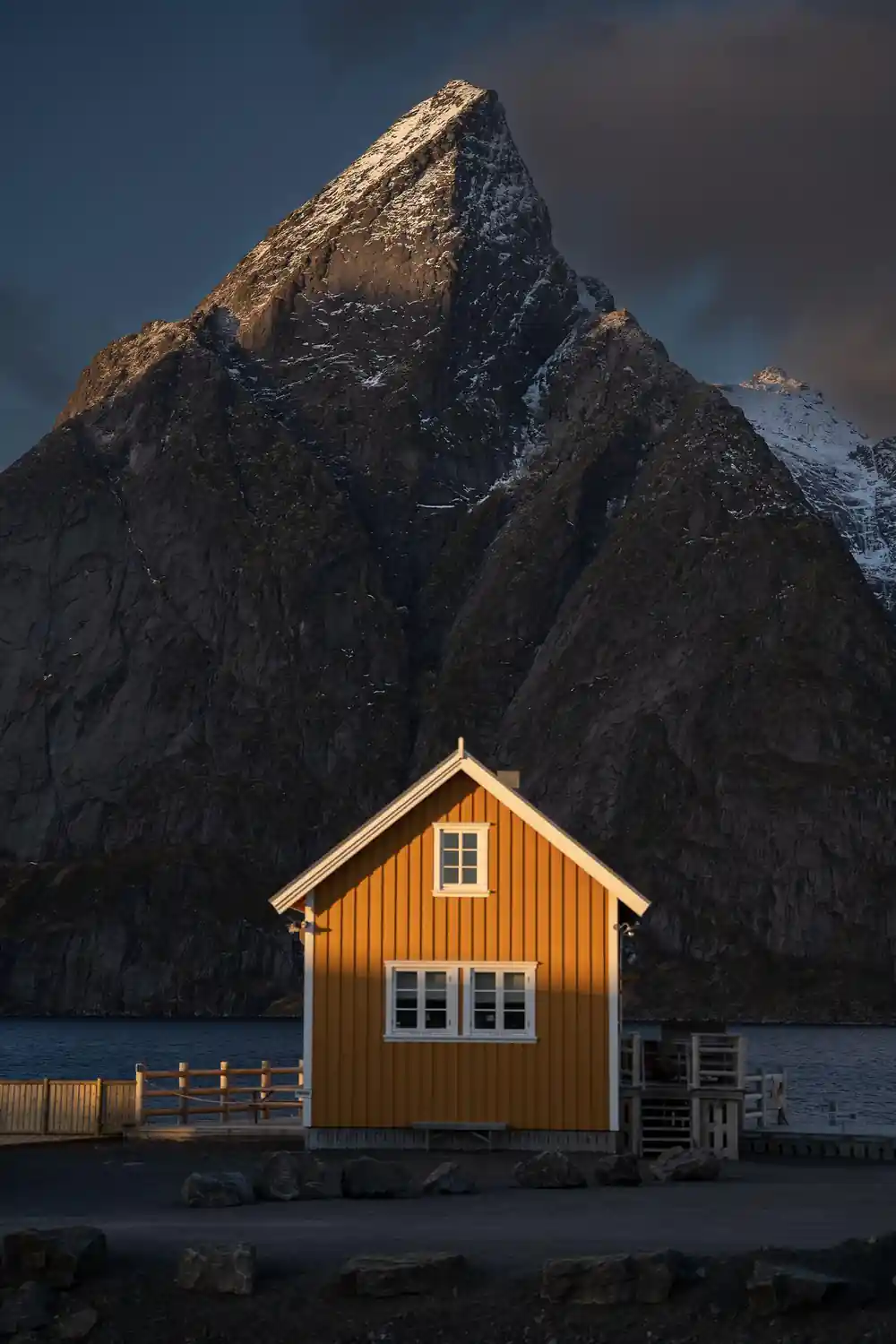 Yellow wooden cabin beneath dramatic dark rocky mountain peak